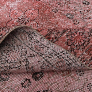 May include: Close-up of a pink and black patterned rug with a floral design. The rug is folded in half, showing the texture and weave of the fabric.