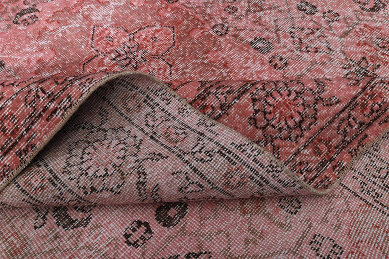 May include: Close-up of a pink and black patterned rug with a floral design. The rug is folded in half, showing the texture and weave of the fabric.