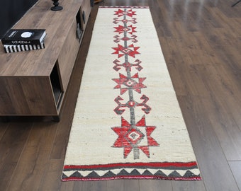 May include: A white runner rug with a red and gray geometric pattern. The rug has a fringe border and is approximately 8 feet long.