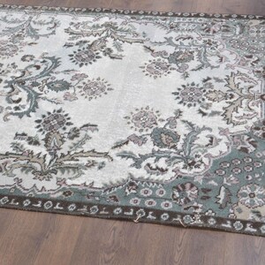 May include: A vintage rug with a floral pattern in shades of green, brown, and white. The rug has a faded, distressed look and a fringed edge.