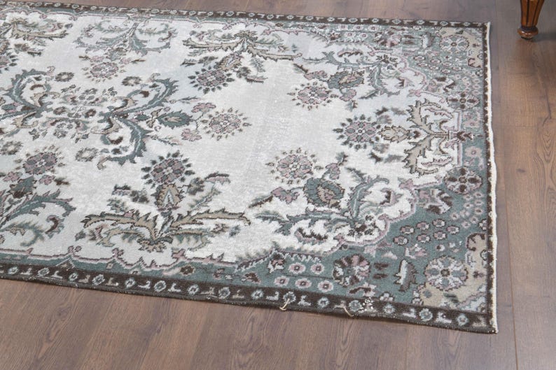 May include: A vintage rug with a floral pattern in shades of green, brown, and white. The rug has a faded, distressed look and a fringed edge.