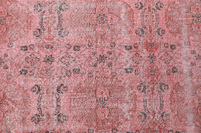 May include: A vintage-style rug with a faded pink background and intricate black floral patterns. The rug has a distressed look, giving it a unique and antique feel.