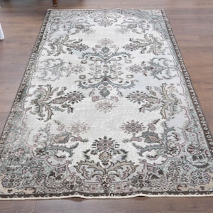 May include: A vintage style rug with a white background and a floral pattern in shades of brown, green, and pink. The rug has a distressed look and a fringed edge.