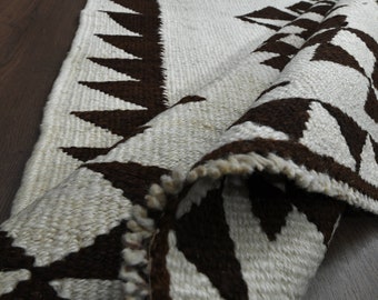 May include: A white and brown woven rug with a geometric pattern. The rug is folded in half and the edges are frayed.