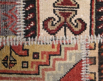 May include: Close-up of a patchwork rug with a variety of geometric and floral patterns. The rug features a combination of colors, including red, beige, black, and gold. The edges are stitched together with a white thread.