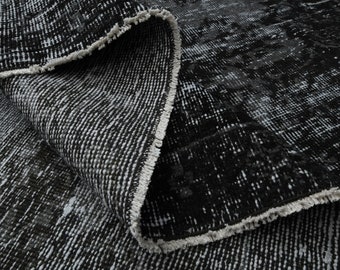May include: Close-up of a black and white patterned rug with a fringed edge. The rug is folded over, showing the texture of the fabric.