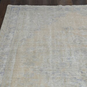 May include: A light beige area rug with a faded, distressed pattern in shades of blue and gray. The rug has a subtle, vintage look.