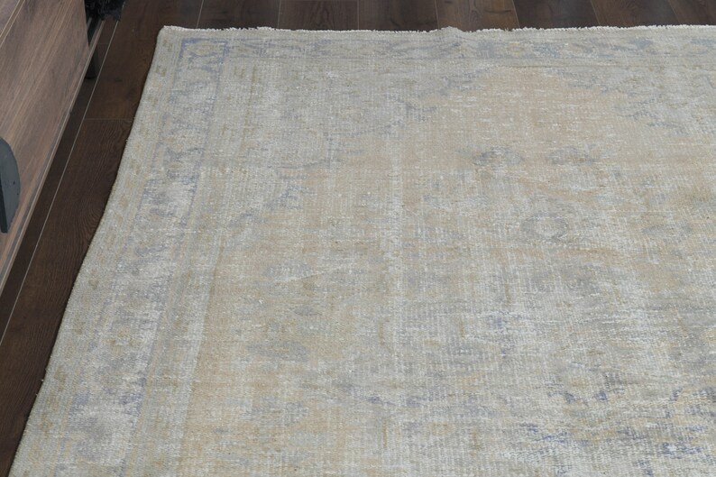 May include: A light beige area rug with a faded, distressed pattern in shades of blue and gray. The rug has a subtle, vintage look.