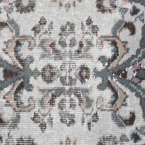 May include: Close-up of a cream-colored rug with a detailed floral pattern in shades of brown, green, and pink.