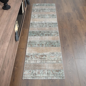May include: A long, rectangular runner rug with a striped pattern in shades of beige, brown, and blue. The rug has a distressed, vintage look.