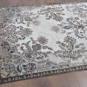 May include: A vintage rug with a floral pattern in shades of brown, green, and pink on a white background. The rug has a distressed look and a dark brown border.