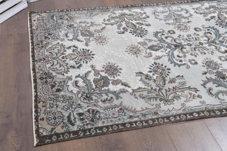 May include: A vintage rug with a floral pattern in shades of brown, green, and pink on a white background. The rug has a distressed look and a dark brown border.