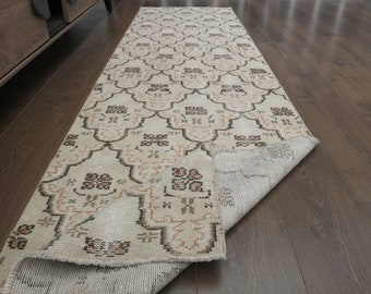 May include: A beige runner rug with a geometric pattern in shades of brown and pink. The rug is folded in half and lying on a wooden floor.