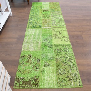 May include: A green patchwork runner rug with various patterns, including floral and geometric designs. The rug is placed on a dark wood floor. The rug's design incorporates different shades of green.