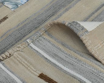 May include: Close-up of a woven rug with beige and gray stripes. The rug has a fringed edge and a textured surface.