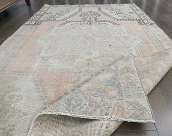 May include: A rectangular, distressed-look rug with a central medallion design. The rug features a muted color palette of beige, peach, and faded blue, with intricate patterns and a slightly rolled-up edge, showcasing its texture.