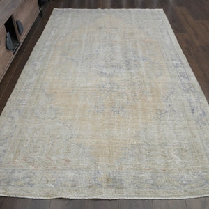 May include: A light beige vintage rug with a faded floral pattern and a light blue border. The rug is laid out on a hardwood floor.