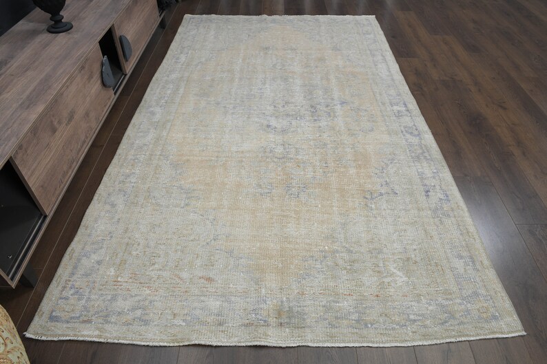 May include: A light beige vintage rug with a faded floral pattern and a light blue border. The rug is laid out on a hardwood floor.