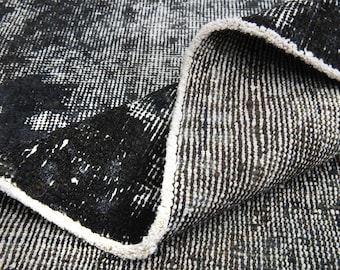 May include: Close-up of a rolled-up, distressed rug. The rug has a black and white pattern with a textured look. The edges have a white border, and the rug appears to be made of a woven material.
