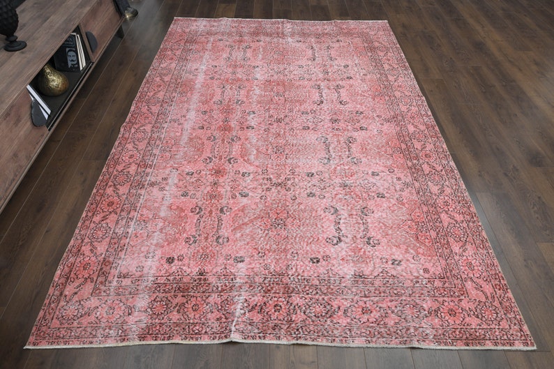 May include: A vintage pink and black patterned rug with a faded look. The rug has a floral design and a border.