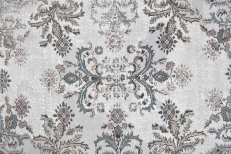 May include: A white rug with a repeating floral pattern in shades of gray, brown, and pink.