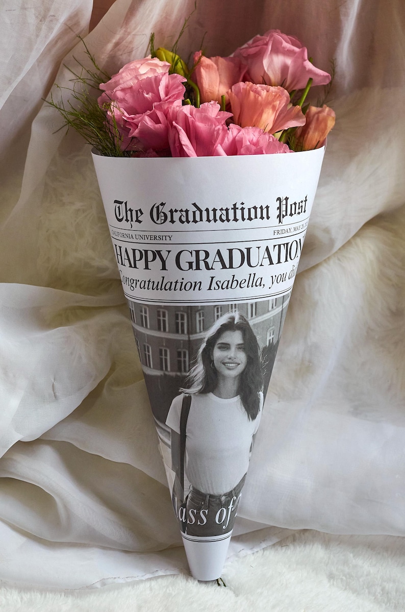 K&ouml;nnte beinhalten: Ein Strau&szlig; rosa Blumen, verpackt in einem Zeitungskegel mit der &Uuml;berschrift "The Graduation Post" und dem Text "HAPPY GRADUATION Congratulation Isabella, you did it!" und "Class of..."