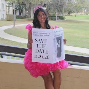 May include: A young person wearing a pink dress and a tiara holds a newspaper-style invitation. The invitation reads "JOIN US TO CELEBRATE SOFIA'S QUINCEA&Ntilde;ERA" and "SAVE THE DATE 11.21.26". The image is taken outdoors.