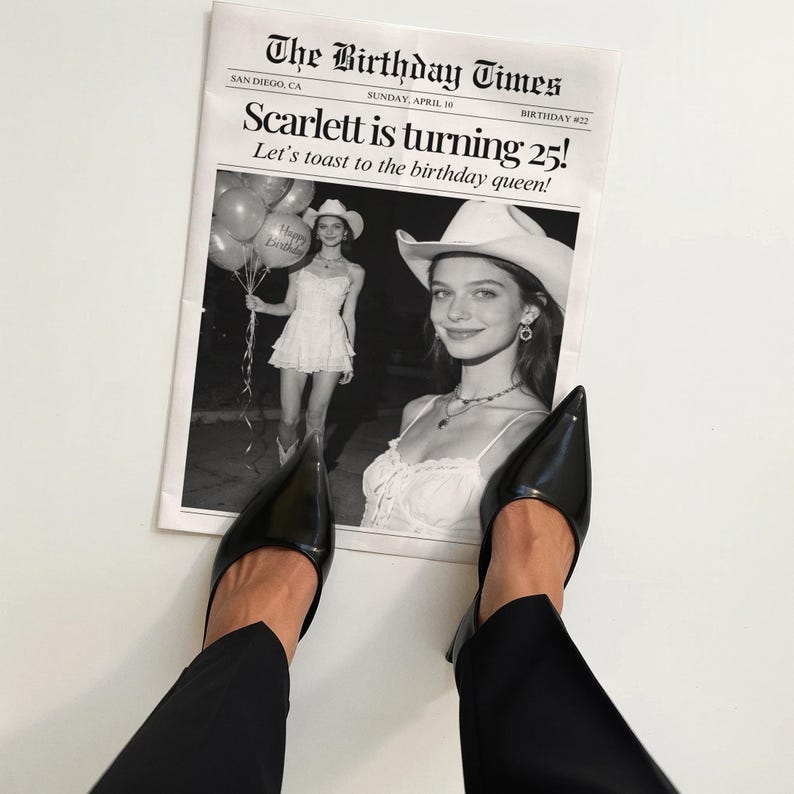 May include: Black pointed-toe pumps and black pants are positioned over a newspaper. The newspaper is titled "The Birthday Times" and features a photo of a woman in a white dress and cowboy hat. The headline reads "Scarlett is turning 25!"