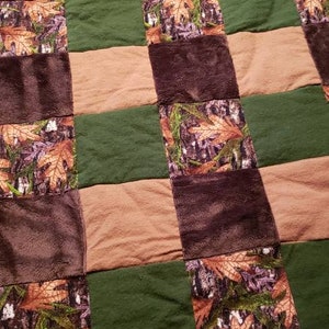 May include: A brown and green patchwork quilt with a camouflage pattern. The quilt is made of squares of different fabrics, including brown, green, and tan.
