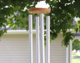 May include: A white wind chime with five metal tubes hanging from a wooden ring. The tubes are suspended by white strings and a wooden block hangs from the bottom of the chime.