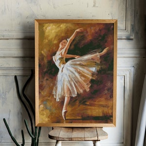 May include: A framed artwork depicting a ballerina in a white tutu, poised mid-leap. The painting features warm tones of gold, brown, and white, with a wooden frame. The artwork is displayed on a small, rustic wooden stool.