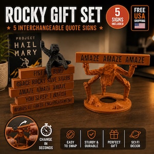 May include: A Rocky gift set featuring five interchangeable quote signs and a black textured alien figure. The set includes a brown stand with a multi-legged alien figure holding a sign that reads AMAZE AMAZE AMAZE. Other signs include FIST BUMP, GRACE ROCKY SAVE STARS, YOU SLEEP, I WATCH, and WORDS OF GREAT ENCOURAGEMENT.