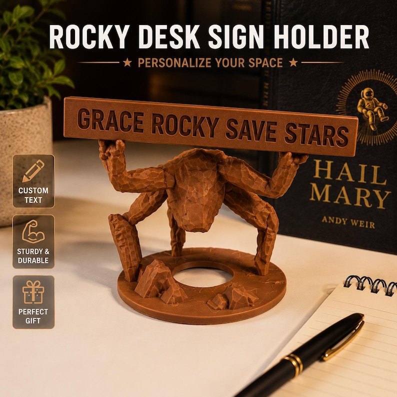 Puede incluir: Un soporte de letrero de escritorio marr&oacute;n texturizado con una criatura de varias patas sobre una base circular con rocas, que sostiene un letrero rectangular horizontal con el texto GRACE ROCKY SAVE STARS en letras may&uacute;sculas.