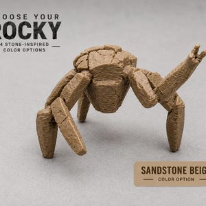 Può includere: Una scultura beige ispirata alla pietra, raffigurante una creatura con più zampe e un corpo segmentato. Il testo "CHOOSE YOUR ROCKY" è in alto, con "4 STONE-INSPIRED COLOR OPTIONS" sotto. L'opzione colore è "SANDSTONE BEIGE".