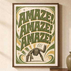 以下が含まれることがあります： 大きなオリーブグリーンの太字で「AMAZE!」という文字が3回繰り返された額入りアートプリント。テキストの下には、質感のある表面を持つ灰色の岩のような多脚の生き物が描かれており、緑と黄色の渦巻く線と小さな星のアクセントが施されたクリーム色の背景に配置されています。