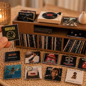 Op de afbeelding: Miniatuur houten platenspeler en een verzameling vinylplaten. Albums van Nirvana, AC/DC, Pink Floyd, The Rolling Stones en meer zijn zichtbaar. Een kleine kaars en een decoratieve vaas zijn ook aanwezig.