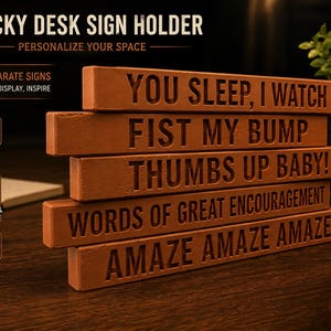 Puede incluir: Un conjunto de cinco letreros de escritorio rectangulares de madera marr&oacute;n apilados verticalmente. Cada letrero presenta texto grabado: YOU SLEEP, I WATCH; FIST MY BUMP; THUMBS UP BABY!; WORDS OF GREAT ENCOURAGEMENT; y AMAZE AMAZE AMAZE.