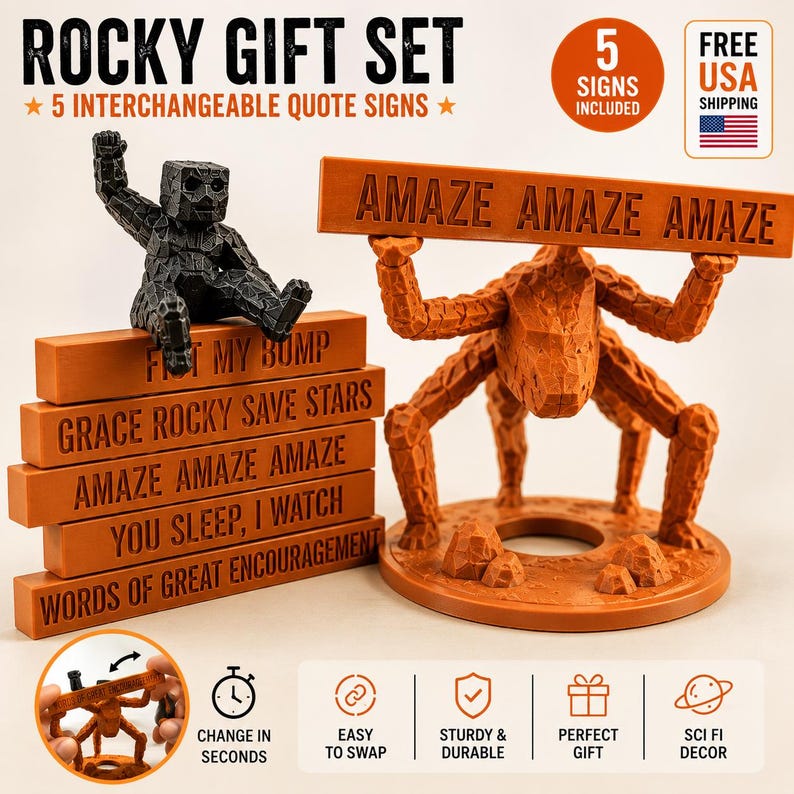 May include: A Rocky gift set featuring a black textured figure sitting on a stack of five orange rectangular signs with the text: FIT MY BUMP, GRACE ROCKY SAVE STARS, AMAZE AMAZE AMAZE, YOU SLEEP, I WATCH, and WORDS OF GREAT ENCOURAGEMENT.