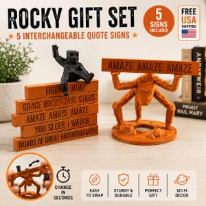 May include: A Rocky gift set featuring five interchangeable orange rectangular signs with black text including FIST ME BUMP, GRACE ROCKY SAVE STARS, AMAZE AMAZE AMAZE, YOU SLEEP I WATCH, and WORDS OF GREAT ENCOURAGEMENT, plus two orange and black figures.