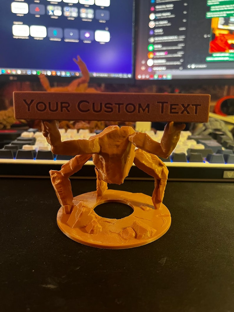 Puede incluir: Una figura de pl&aacute;stico naranja impresa en 3D con textura rocosa, de pie sobre una base circular y sosteniendo una barra horizontal rectangular sobre su cabeza. La barra presenta el texto en relieve "YOUR CUSTOM TEXT".