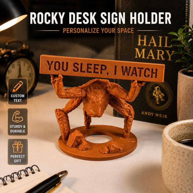 Puede incluir: Un soporte para letreros de escritorio de color marr&oacute;n con textura, que presenta una figura esculpida con m&uacute;ltiples extremidades que sostiene una placa rectangular horizontal. La placa tiene el texto "YOU SLEEP, I WATCH" en may&uacute;sculas.