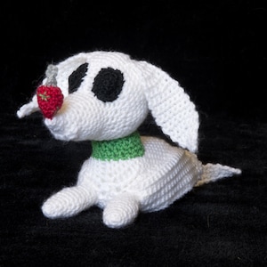 May include: White crocheted dog toy with black eyes and a red strawberry in its mouth. The dog is wearing a green collar.