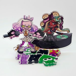 May include: A purple and white cartoon character holding a microphone stands next to a red cartoon character with purple hair holding a record player. The characters are on a black and white background with a green and purple design.