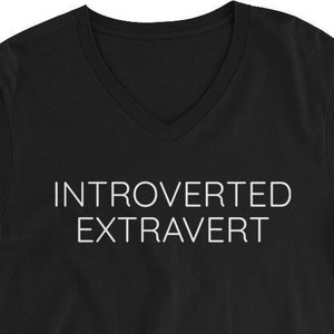 Può includere: Maglietta nera a collo a V con la scritta "Introverso Estroverso" stampata in bianco sul davanti.