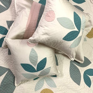 May include: White bedding set with a floral design. The set includes a quilt and square pillows. The quilt and pillows feature teal, light blue, pink, and gold leaf and circle designs. The pillows have a quilted texture.