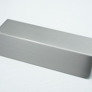 May include: A brushed stainless steel cabinet pull with a rectangular shape and rounded edges.