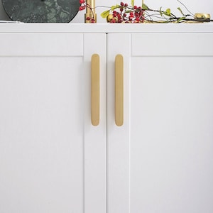 Op de afbeelding: Twee rechthoekige gouden kastgrepen. De grepen zijn gemonteerd op een witte kastdeur.