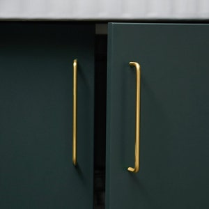 Peut inclure: Deux portes de placard vert foncé avec des poignées en métal doré. Les portes sont fermées et les poignées sont verticales.