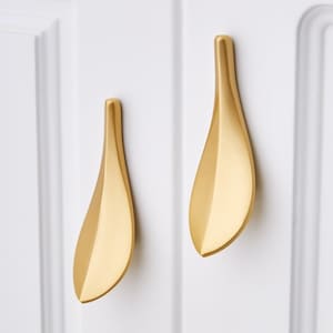 May include: Two gold leaf-shaped cabinet pulls, each with a smooth, rounded surface and a pointed tip.