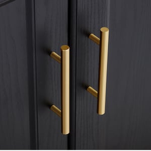 Pode incluir: Duas puxadores de armário douradas com forma cilíndrica. Os puxadores estão montados em uma porta de armário preta.